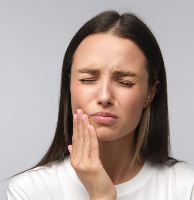 Toothache concept. Studio shot of young female feeling pain, holding her cheek with hand, suffering from bad tooth ache